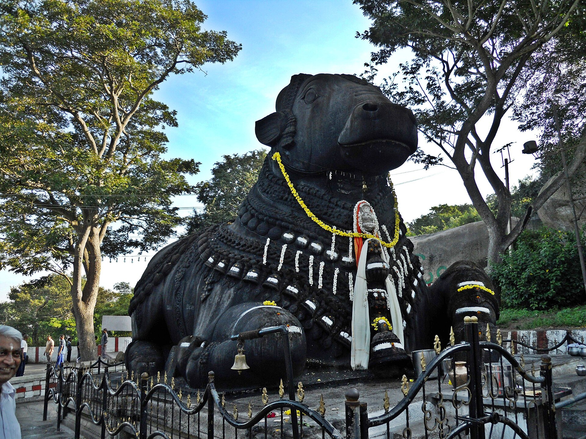 The large black granite Nandi bull on Chamundi Hill, garlanded with flowers under trees